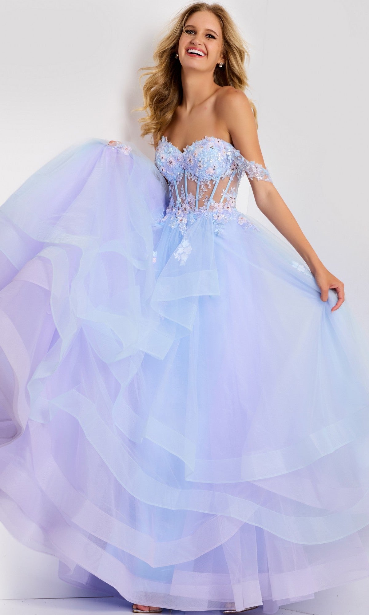 A woman smiles against a plain background wearing the Jovani 47427 long prom dress in lilac, featuring a strapless design, floral appliques, and a voluminous tulle skirt.